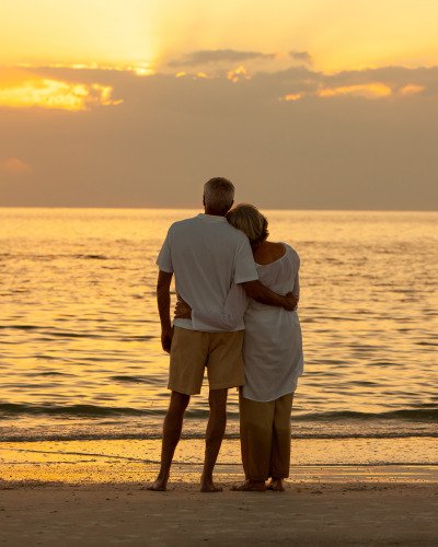 Senior couple from Knoxville embracing on the beach, gazing into the ocean, with the tranquility ensured by our insurance.